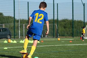 Young person in football kit, kicking a football on a green pitch