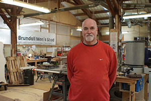 A man standing in a workshop, with Brundall Men's Shed sign on the wall