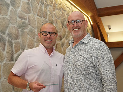 Two men standing on a standing smiling at the camera. One man holding an award
