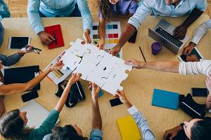 Business professionals around a table holding up large pieces of a jigsaw