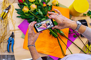 Bunch of bright coloured flowers with a florist taking a photo of them on a phone