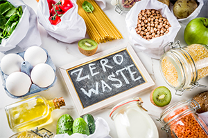 Vegetables, pulses, milk, eggs, fruit and pasta laid out on a table with a chalkboard sign in the middle with zero waste written on it