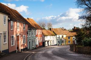 A row of older houses in different colours on a street, with blue skies behind and a tree on the right