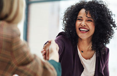 A woman smiling and shaking hands with another woman interviewing her