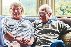 Older lady and man sat on their sofa at home laughing