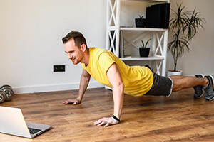 Young man doing push ups in his lounge watching a virtual fitness class