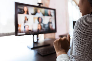 Woman sat at a desk with a computer in front of her on a virtual zoom meeting