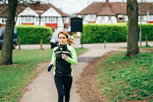 Woman running through a park with houses behind her