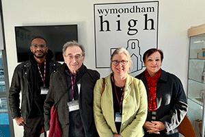 Three people standing in front of a wall sign saying Wymondham High