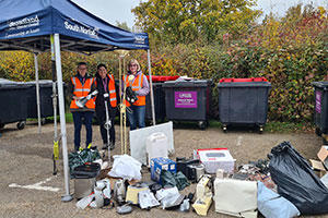 Three ladies in high vis jackets, standing under a tent with piles of electrical items.
