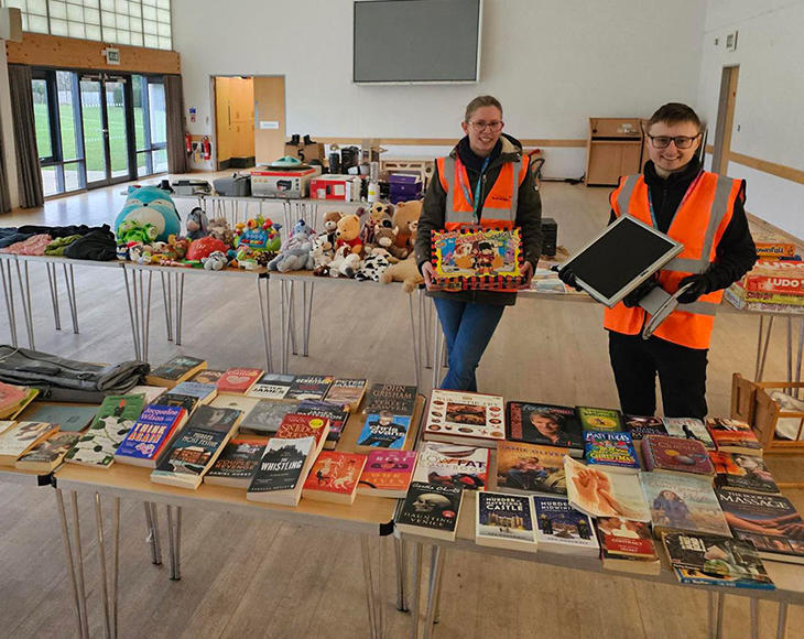 Two recycling officers at a reuse event with tables of books, toys, electricals and textiles