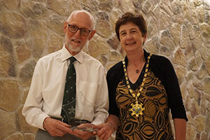 Man in shirt and tie, standing next to the Chair of South Norfolk Council, holding an award and smiling at the camera