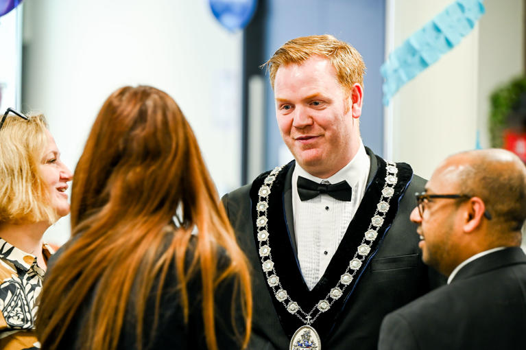 Man in black tie and ceremonial chains chatting to guests.