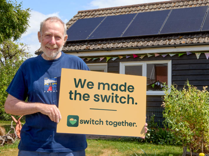 Man holding a Switch Together sign outside a bungalow with solar panels