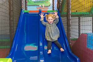 Young girl going down a small slide in a soft play centre
