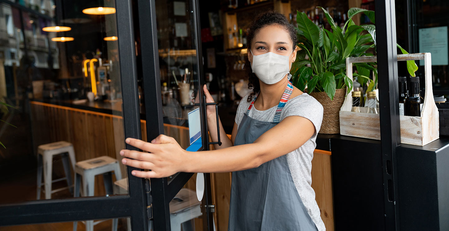 Lady working at a cafe standing in the doorway with a face mask on