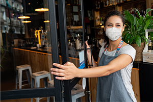 Young woman with a face mask on standing at the door of a cafe