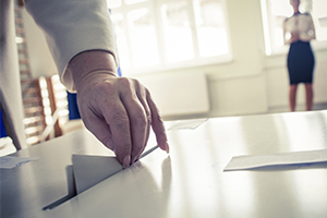 A womans hand putting a ballot paper into a ballot box at an election
