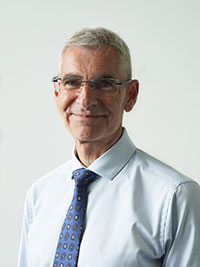 photo of man smiling at camera, with white shirt, blue tie and glasses