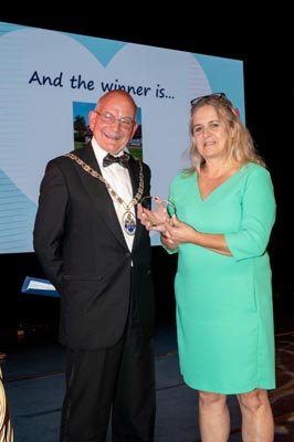 Chairman in a black suit with a bow tie presenting an award to a woman in a green dress
